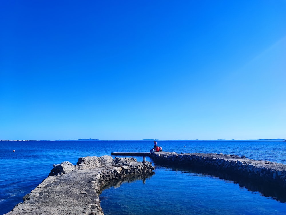 a person sitting on a dock in the middle of a body of water