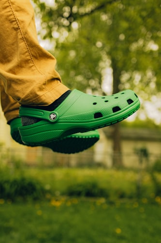 A person wearing a bright green clog shoe while walking in a sunny park