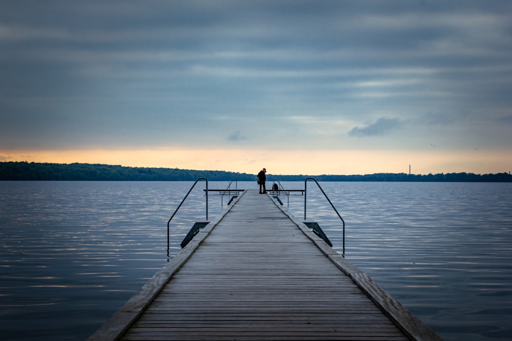 a man standing on a dock at the end of a body of water
