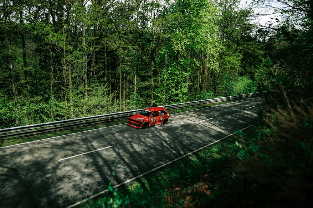 a red car driving down a road next to a forest