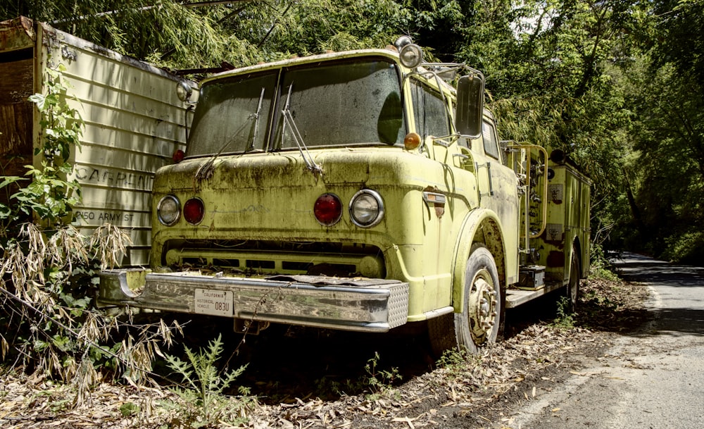 an old yellow truck parked on the side of a road