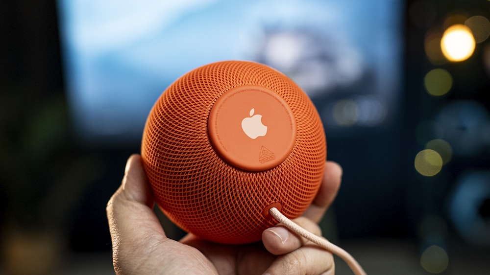 a person holding an orange speaker in front of a tv