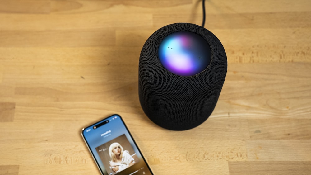 a smart speaker next to an iphone on a wooden table