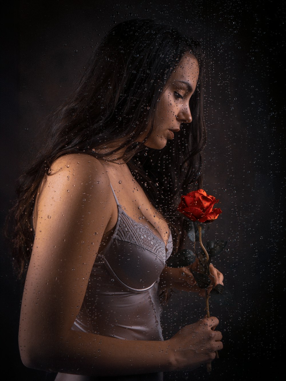 a woman holding a red rose in the rain