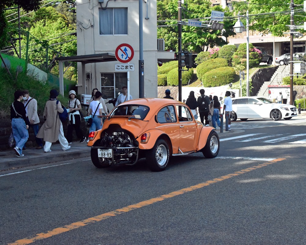 an orange car driving down a street next to a crowd of people