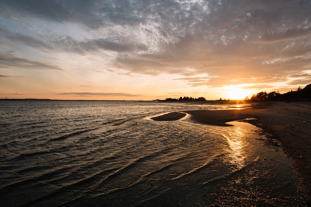 the sun is setting over the water at the beach