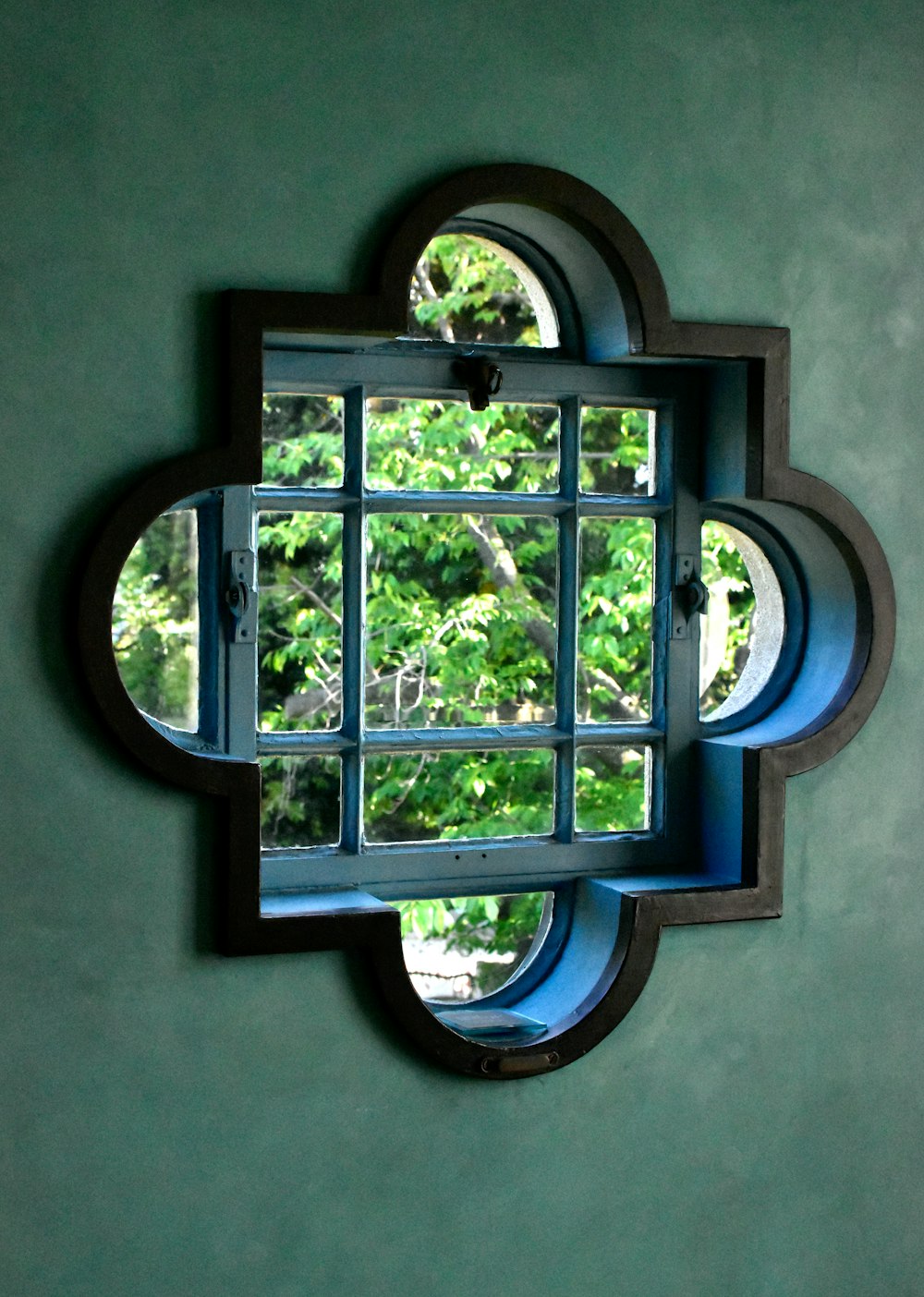 a window in a green wall with a reflection of trees in it