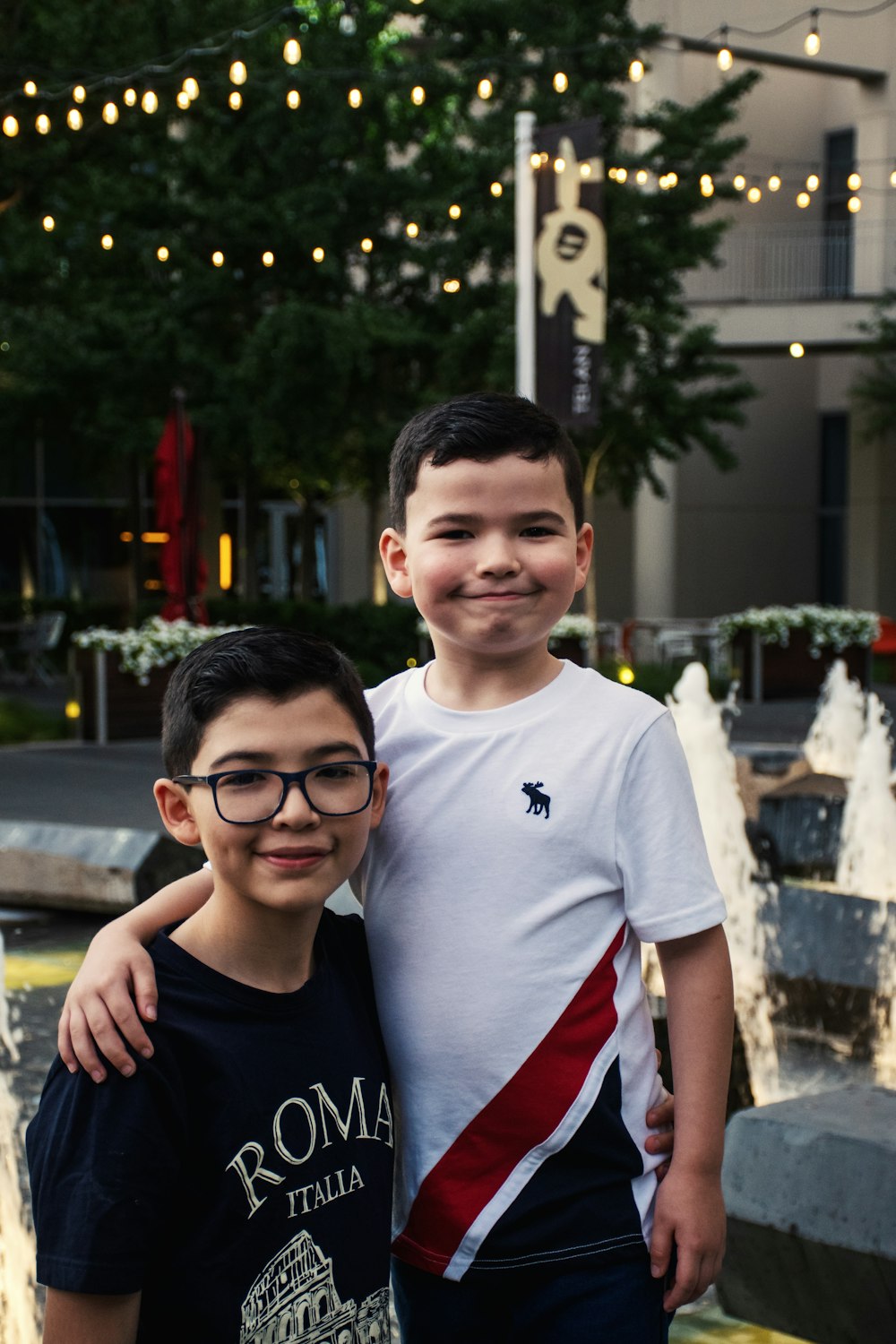 two boys standing next to each other in front of a fountain
