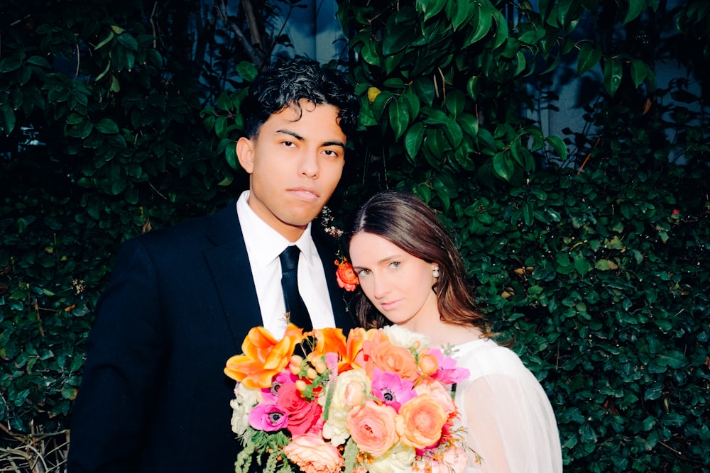 a man and a woman standing next to each other holding a bouquet of flowers