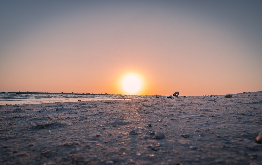 the sun is setting on the beach with footprints in the sand