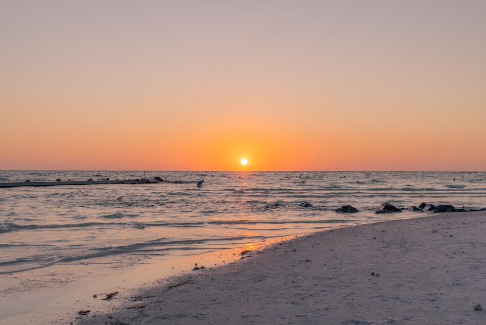 the sun is setting over the water at the beach