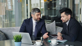a couple of men sitting at a table in front of a laptop