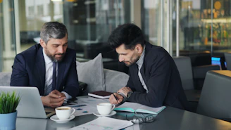 two men sitting at a table working on a laptop