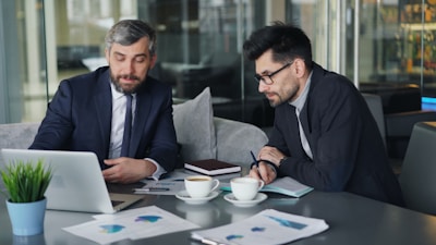 two men sitting at a table working on a laptop