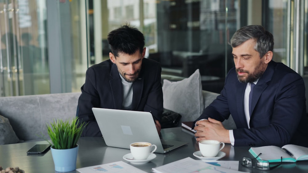 two men sitting at a table looking at a laptop