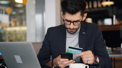 a man sitting at a table looking at his cell phone and holding a credit card