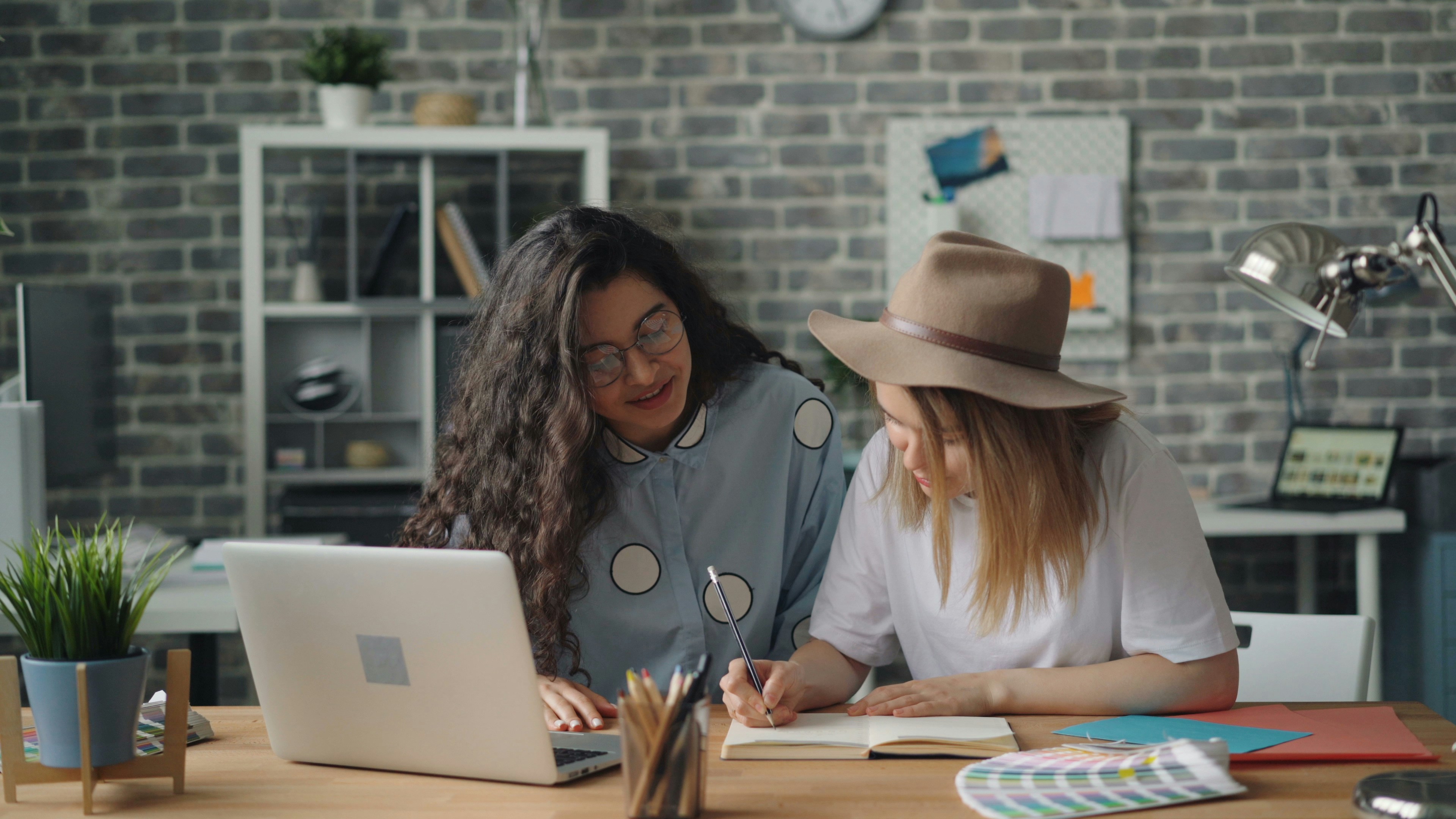dua wanita duduk di meja mengerjakan laptop