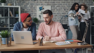 two men sitting at a table with a laptop