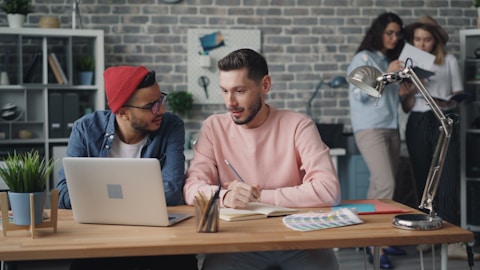 two men sitting at a table with a laptop