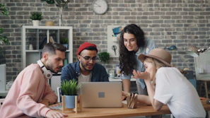 a group of people sitting around a table looking at a laptop