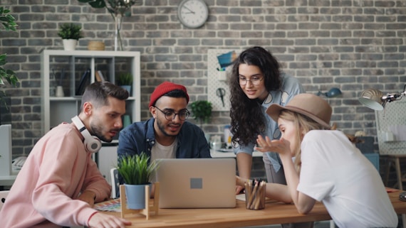 a group of people sitting around a table looking at a laptop