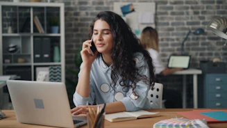 a woman sitting at a desk talking on a cell phone