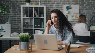 a woman sitting at a desk talking on a cell phone