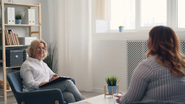 a woman sitting in a chair talking to another woman
