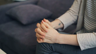 a woman sitting on a couch holding her hands together