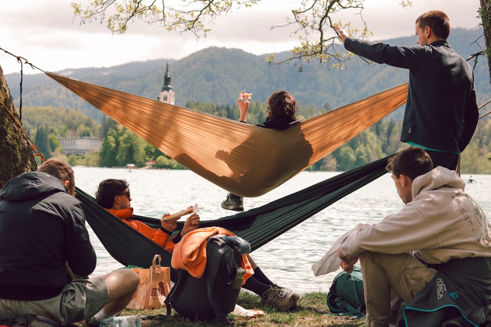 a group of people sitting in a hammock by a lake