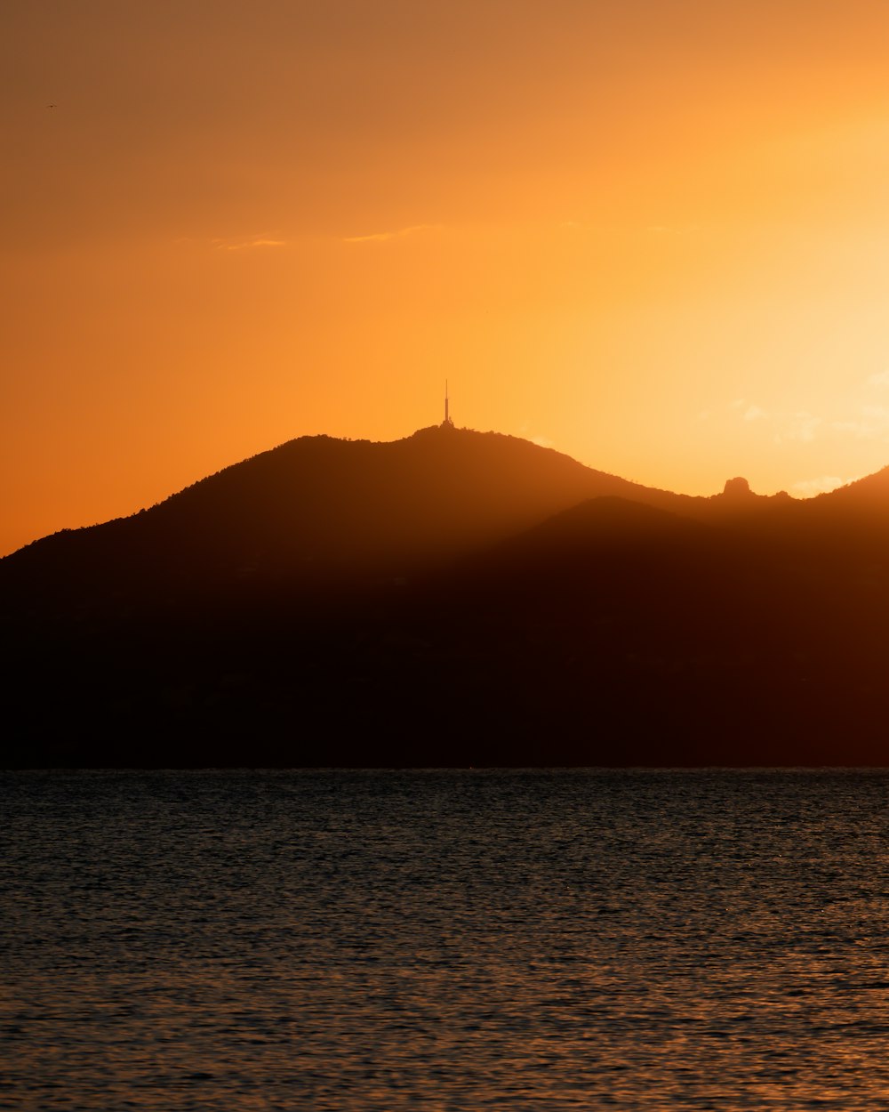 the sun is setting over a mountain with a body of water