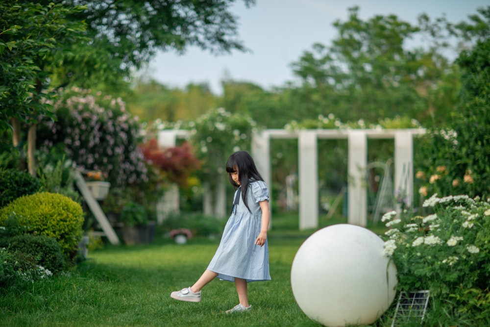 a girl in a blue dress walking through a garden