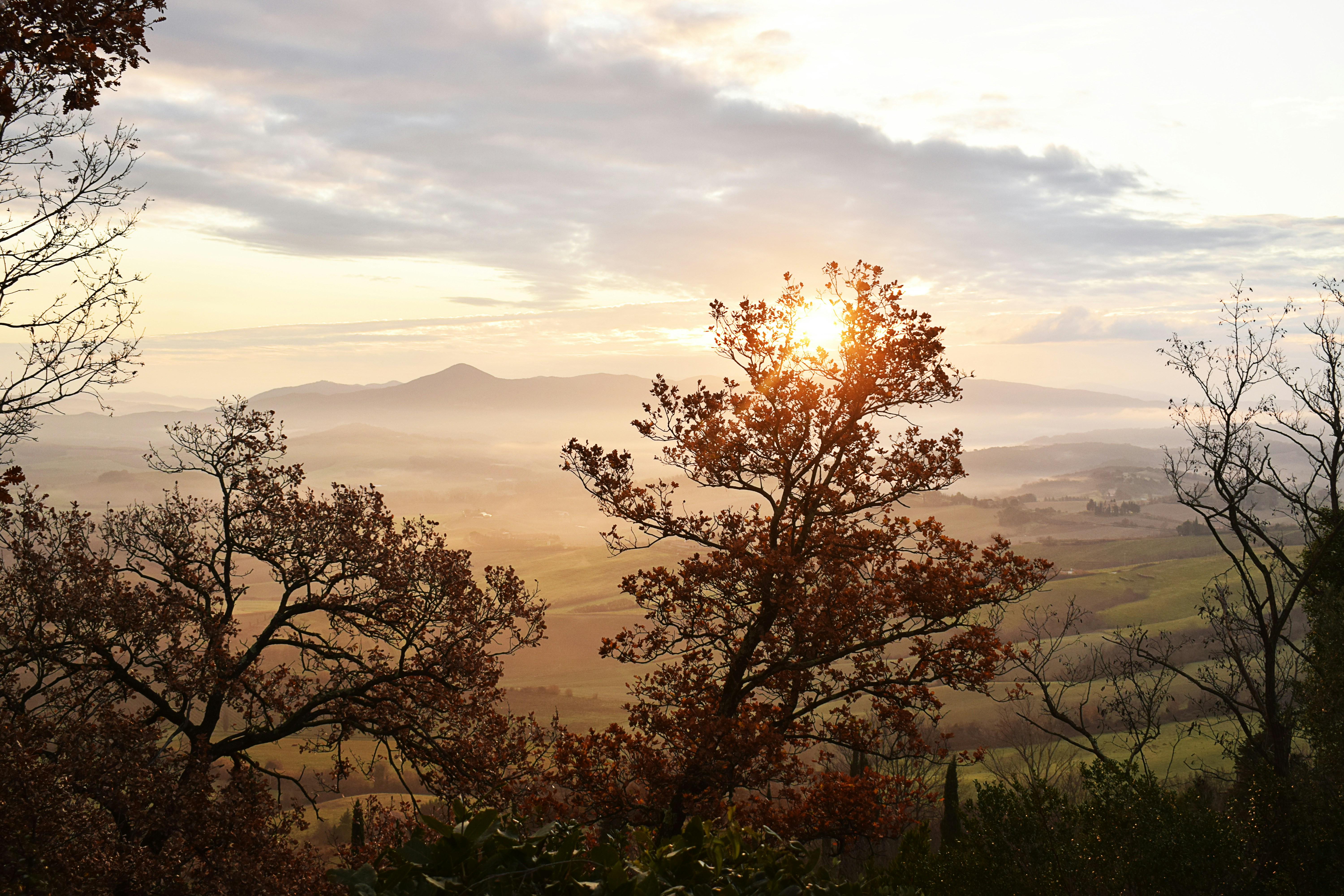 The sun shines through the clouds over a valley