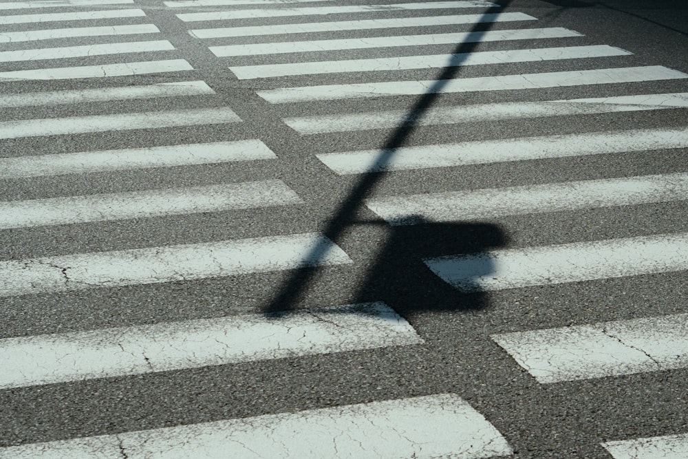 Der Schatten eines Straßenschilds auf einem Zebrastreifen