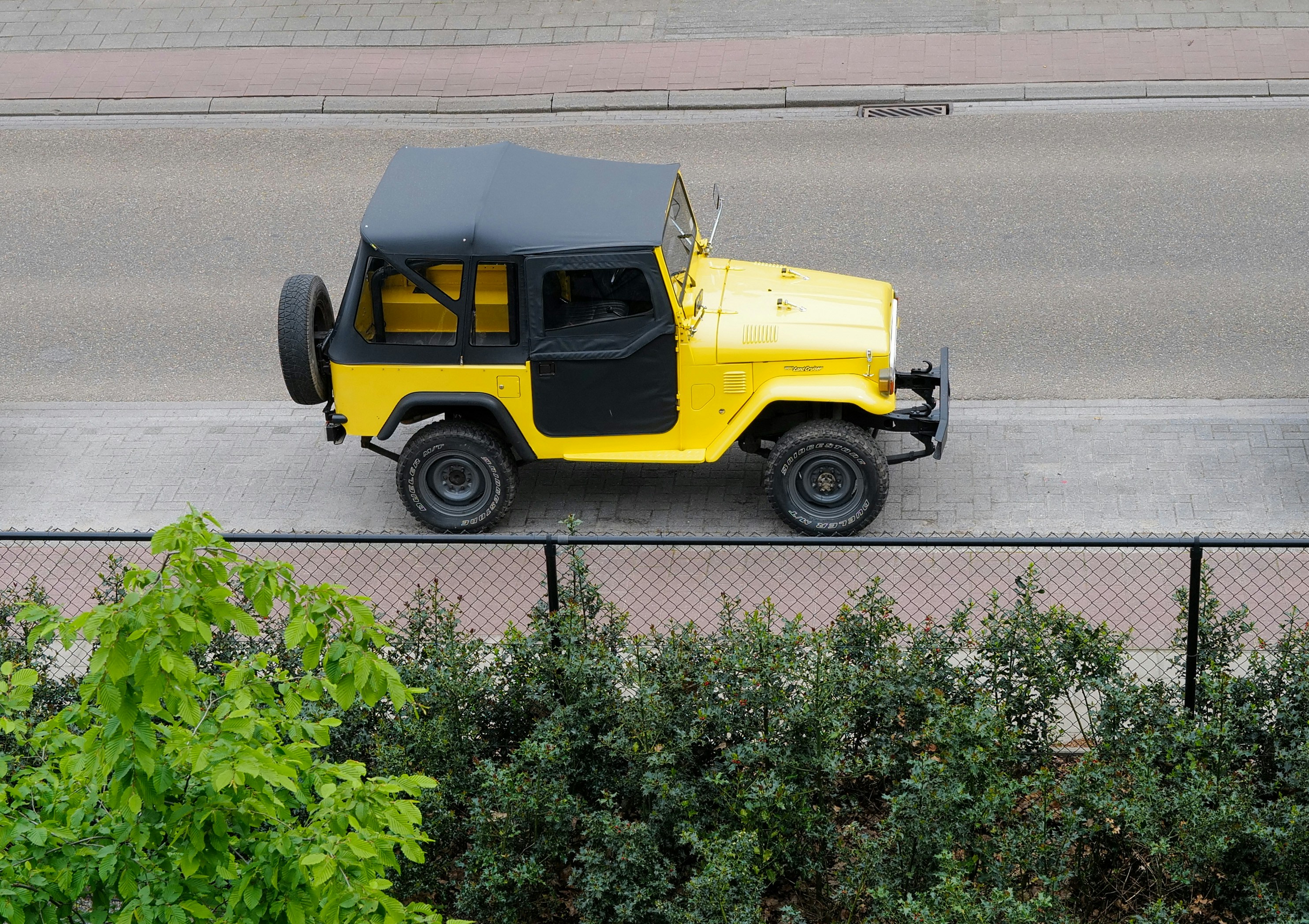 Ein gelber Jeep fährt eine Straße neben einem Zaun hinunter