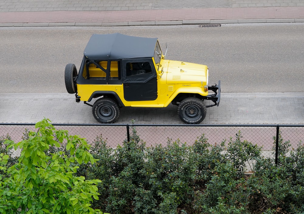 a yellow jeep driving down a street next to a fence
