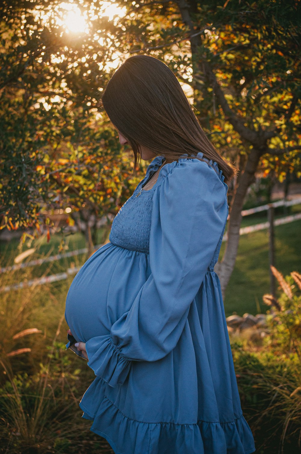 a pregnant woman in a blue dress standing in a field