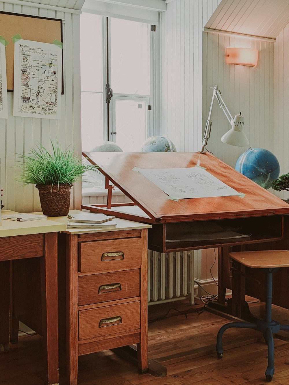 a wooden desk topped with a wooden chair next to a window