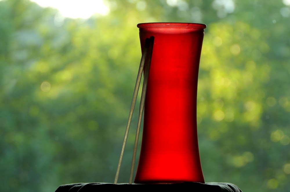 a red vase sitting on top of a table next to a window