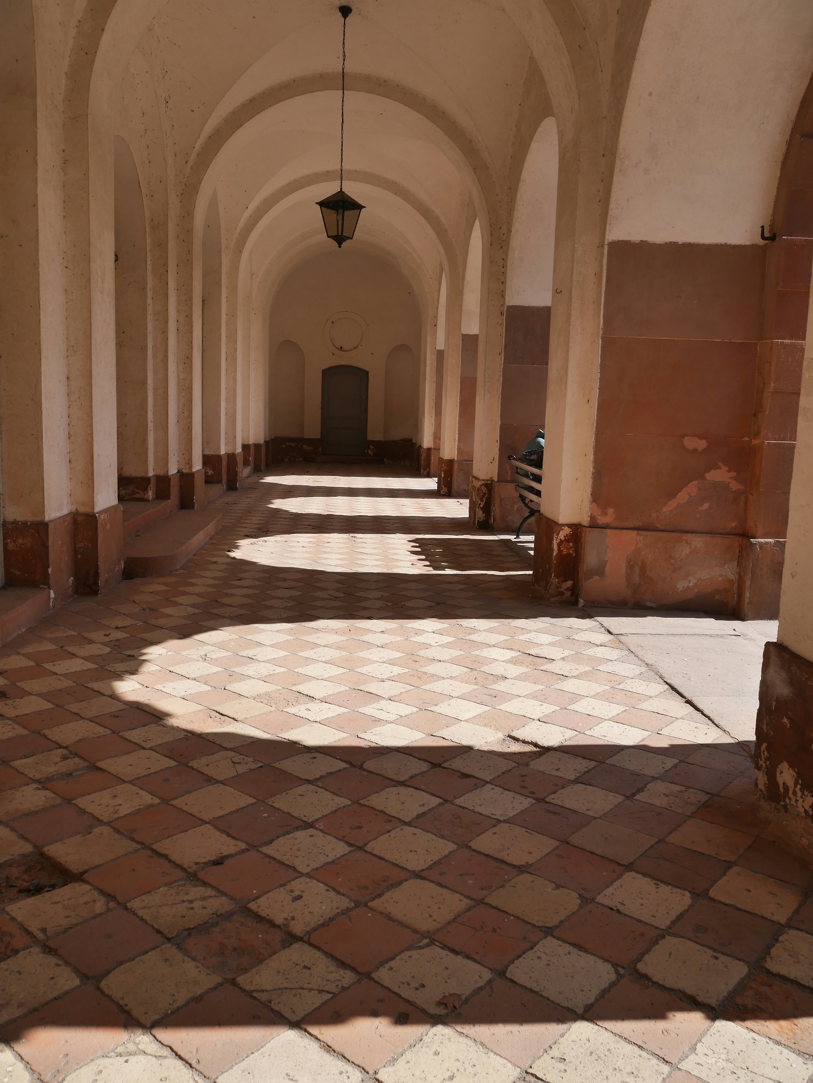 ein langer Flur mit kariertem Boden und einer von der Decke hängenden Laterne