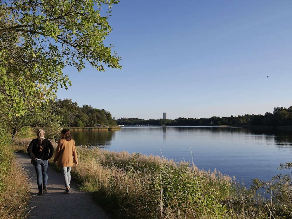 two people walking down a path next to a lake