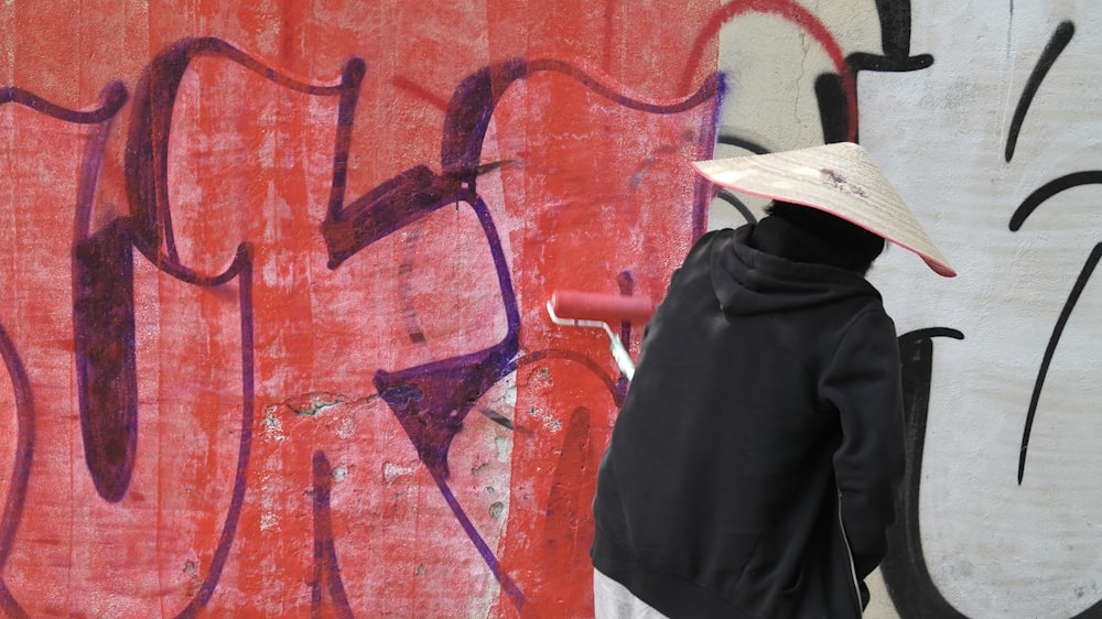a person with a hat standing in front of a wall with graffiti