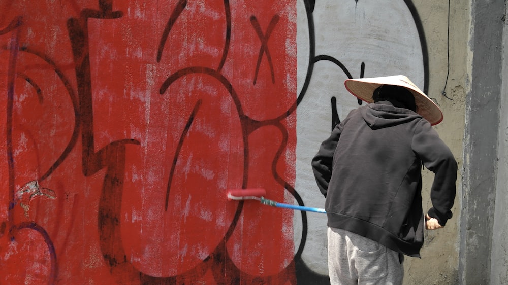 a person with a hat and a stick in front of a wall with graffiti