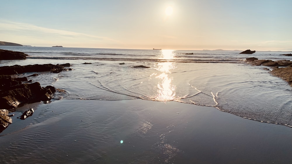 the sun is shining over the water on the beach