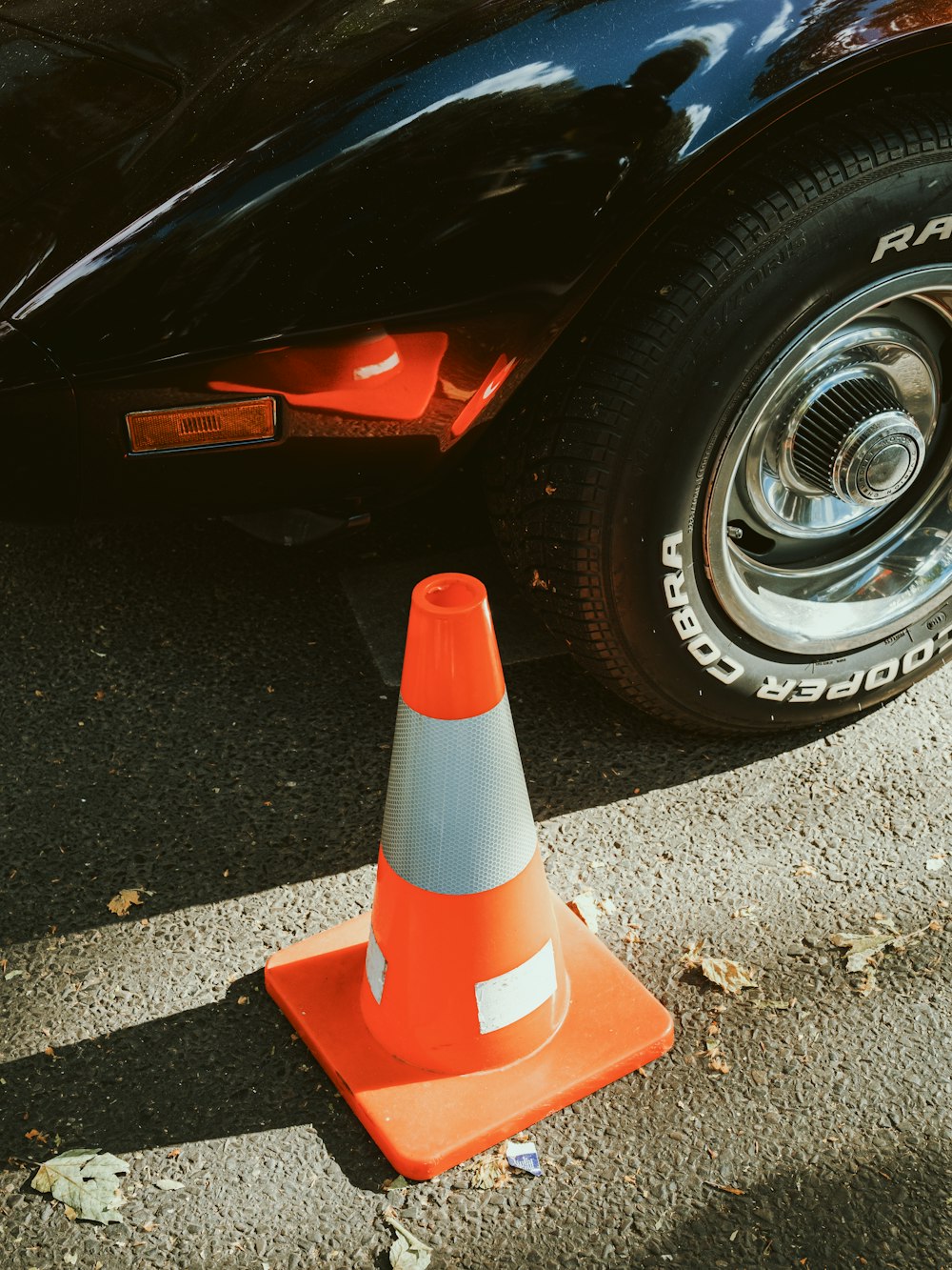 an orange traffic cone sitting next to a black car