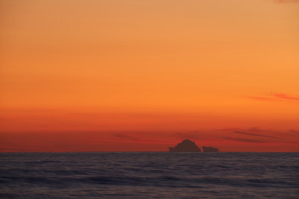 an orange sky with a small island in the middle of the ocean