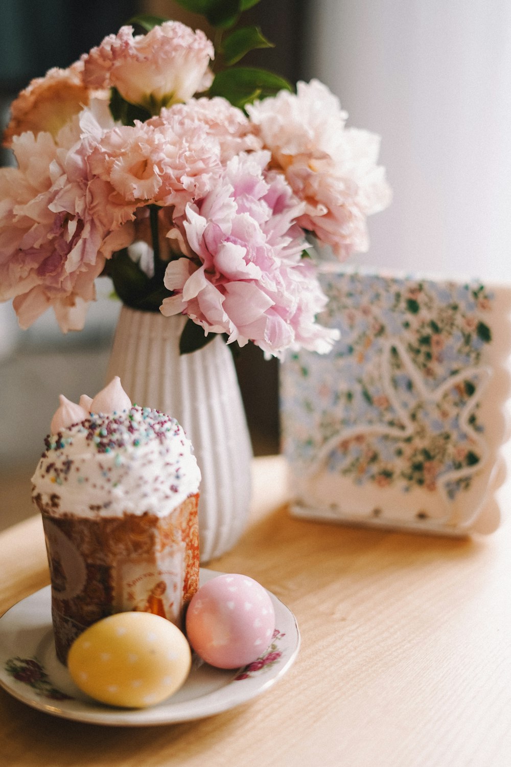 a plate with a cupcake on it next to a vase with flowers