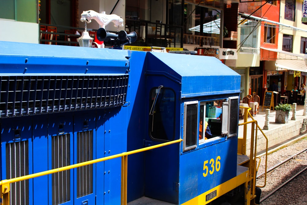 un train bleu circulant sur les voies ferrées à côté d’un grand immeuble