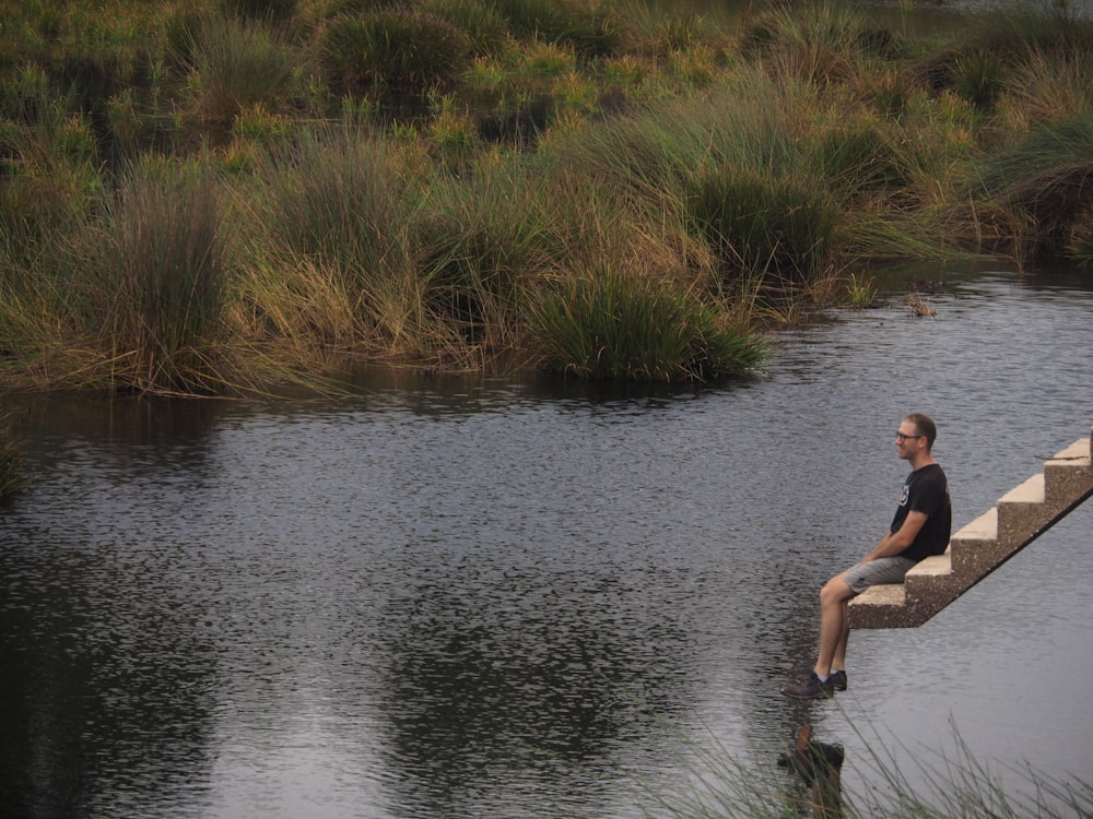 a man sitting on a concrete ledge over a river