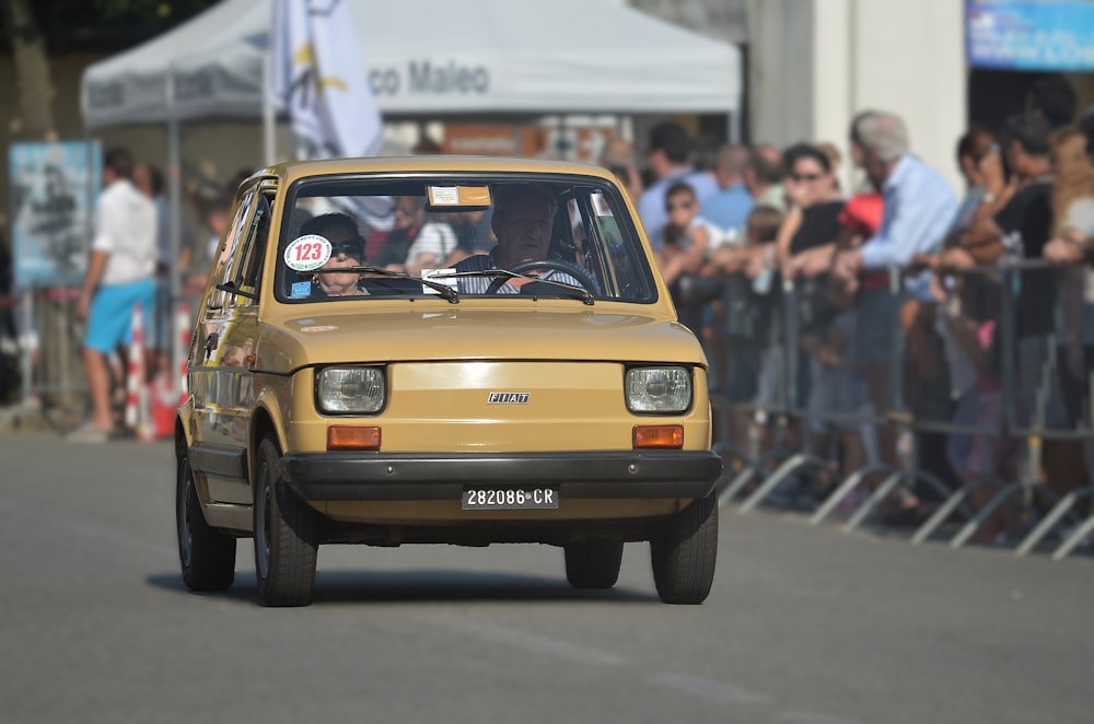 a yellow car driving down a street next to a crowd of people